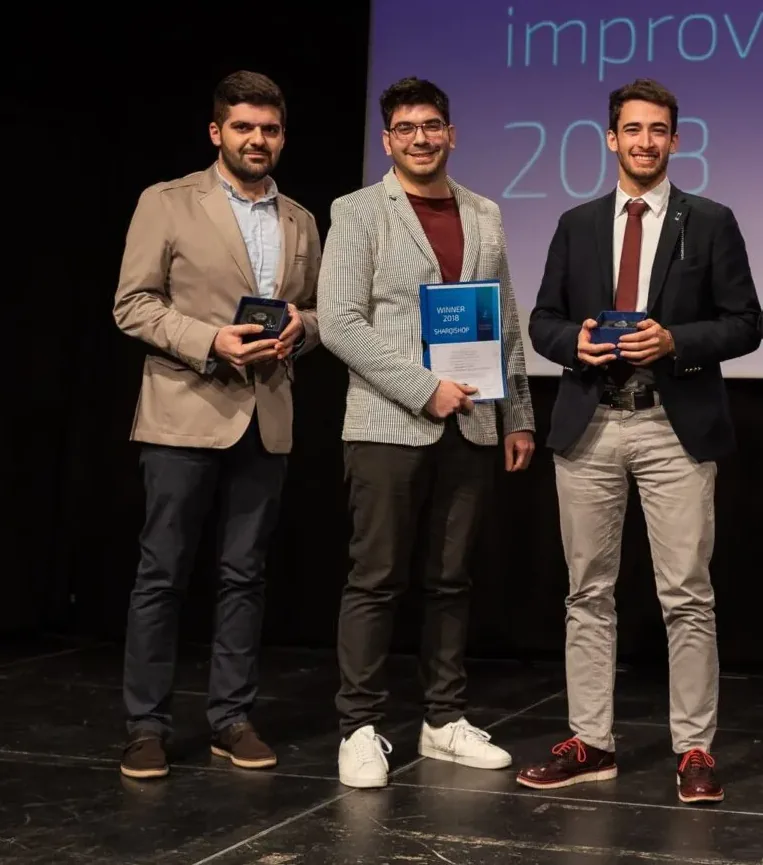 Three co-founders on stage at the European Youth Award 2018 gala, each holding an award box, one holding a winner's certificate, with the ceremony backdrop behind them
