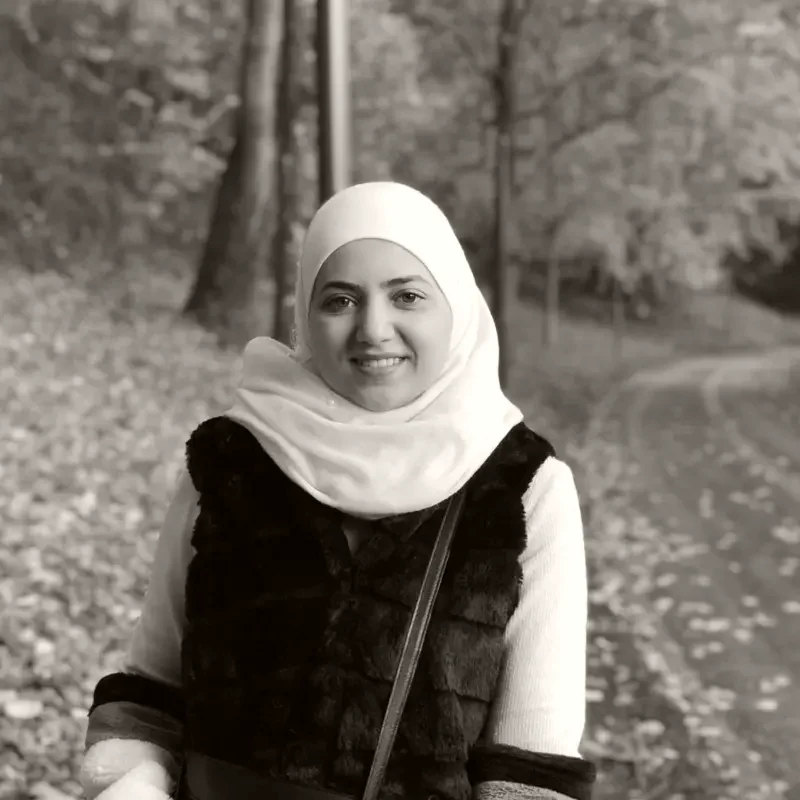 Asmaa Baghdadi, in a cream headscarf, standing on a woodland path