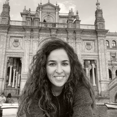 Noora Shanak, smiling, outdoors in front of a colonnaded building