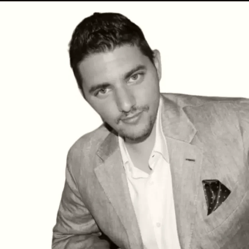 Tareq Malas, in a light blazer and open collar, against a plain bright background