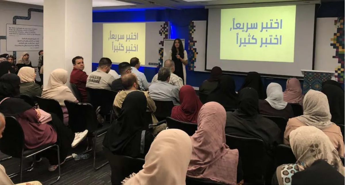 A full room of business owners seated facing a presenter and two screens reading test fast, test often in Arabic