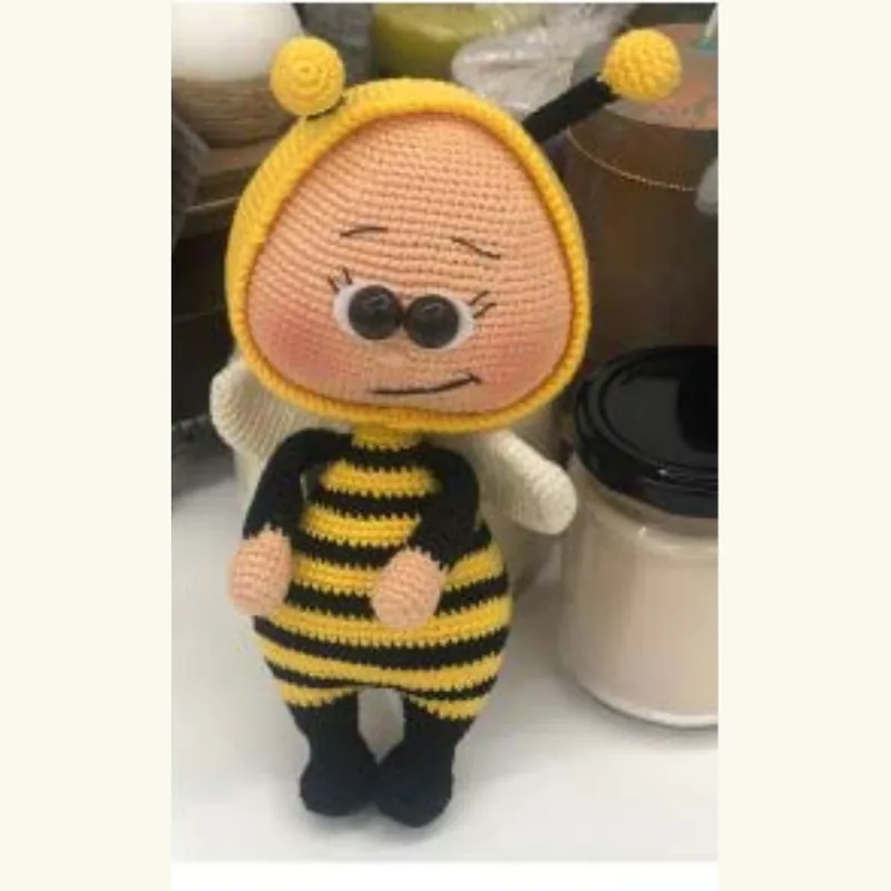 A crocheted doll in a bee costume with hard plastic eyes, photographed on a kitchen counter