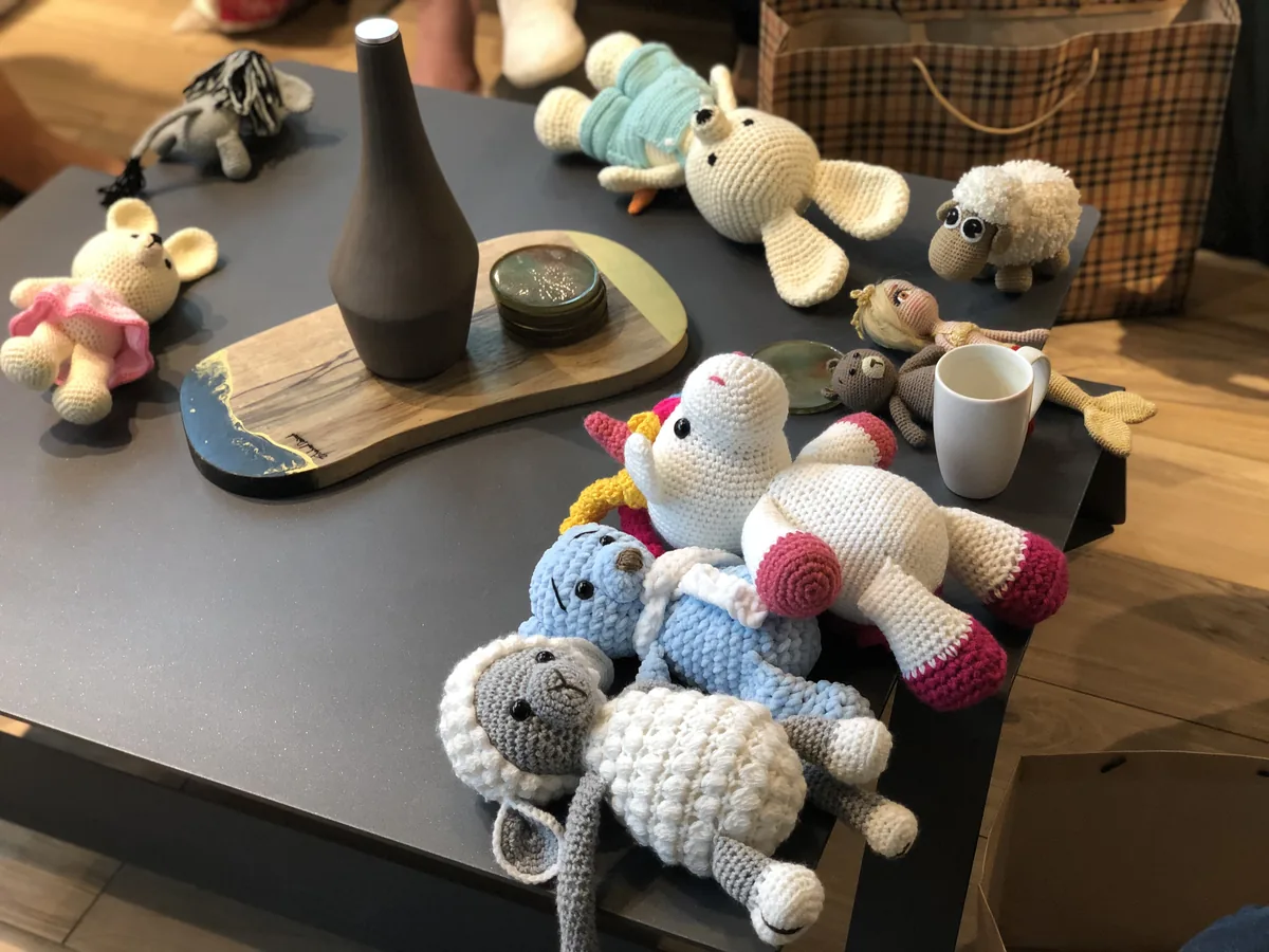 A table covered with handmade crocheted toys — sheep, rabbits, bears and dolls — produced by programme participants